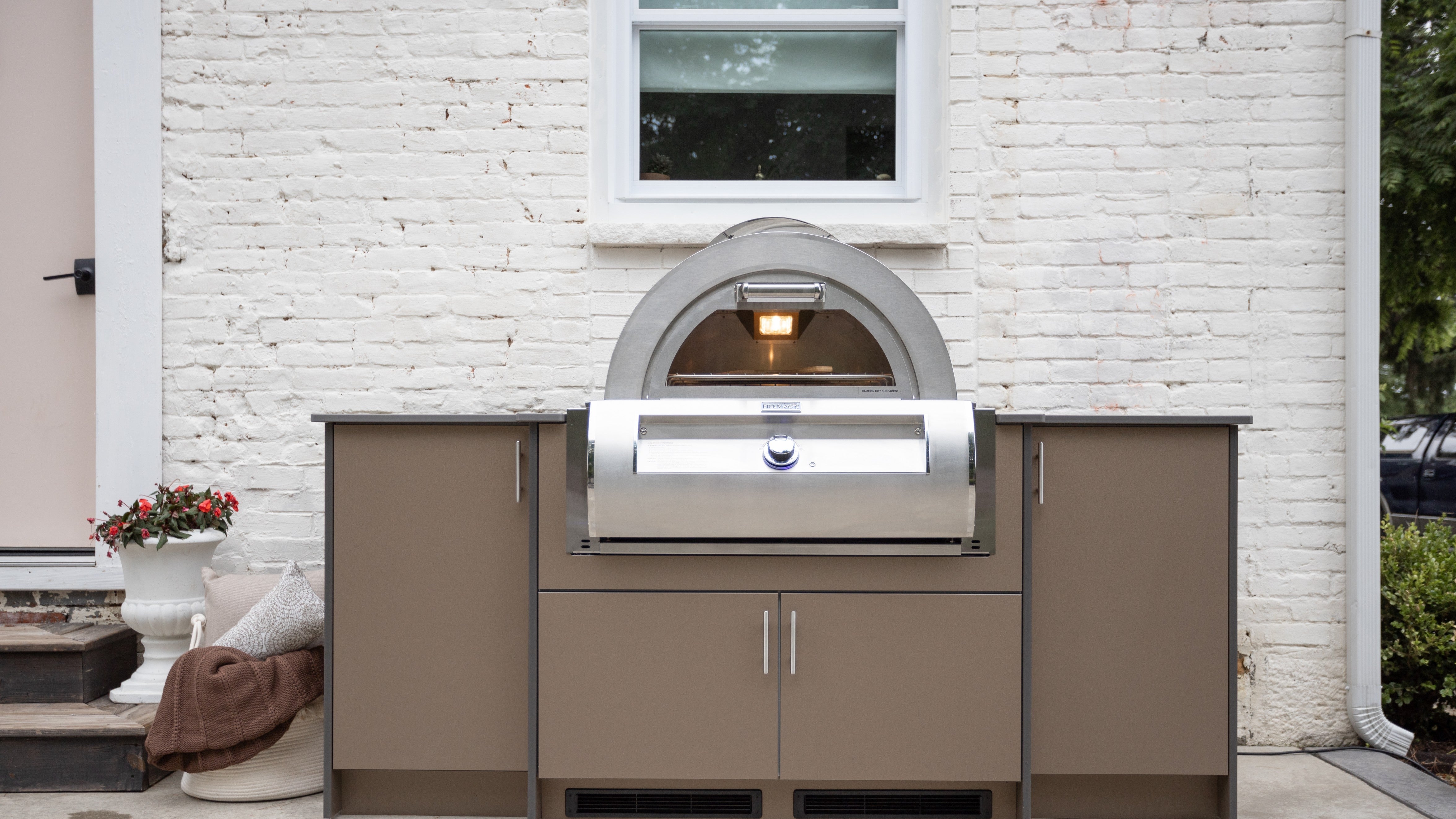 Outdoor kitchen against a brick wall featuring a built-in grill and brown storage cabinets.